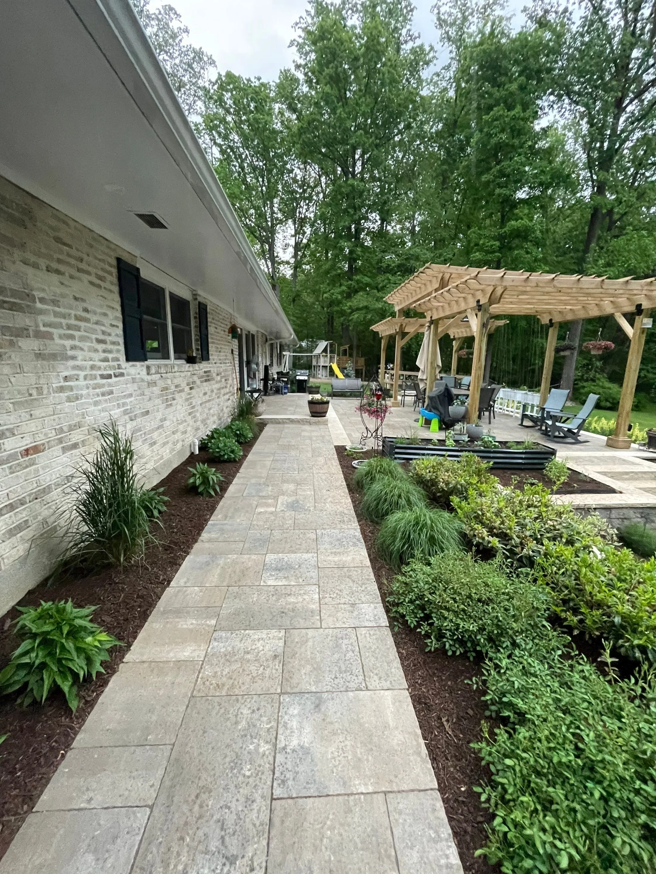 Stone walkway through layered perennial gardens connecting the home to an outdoor pergola and seating area