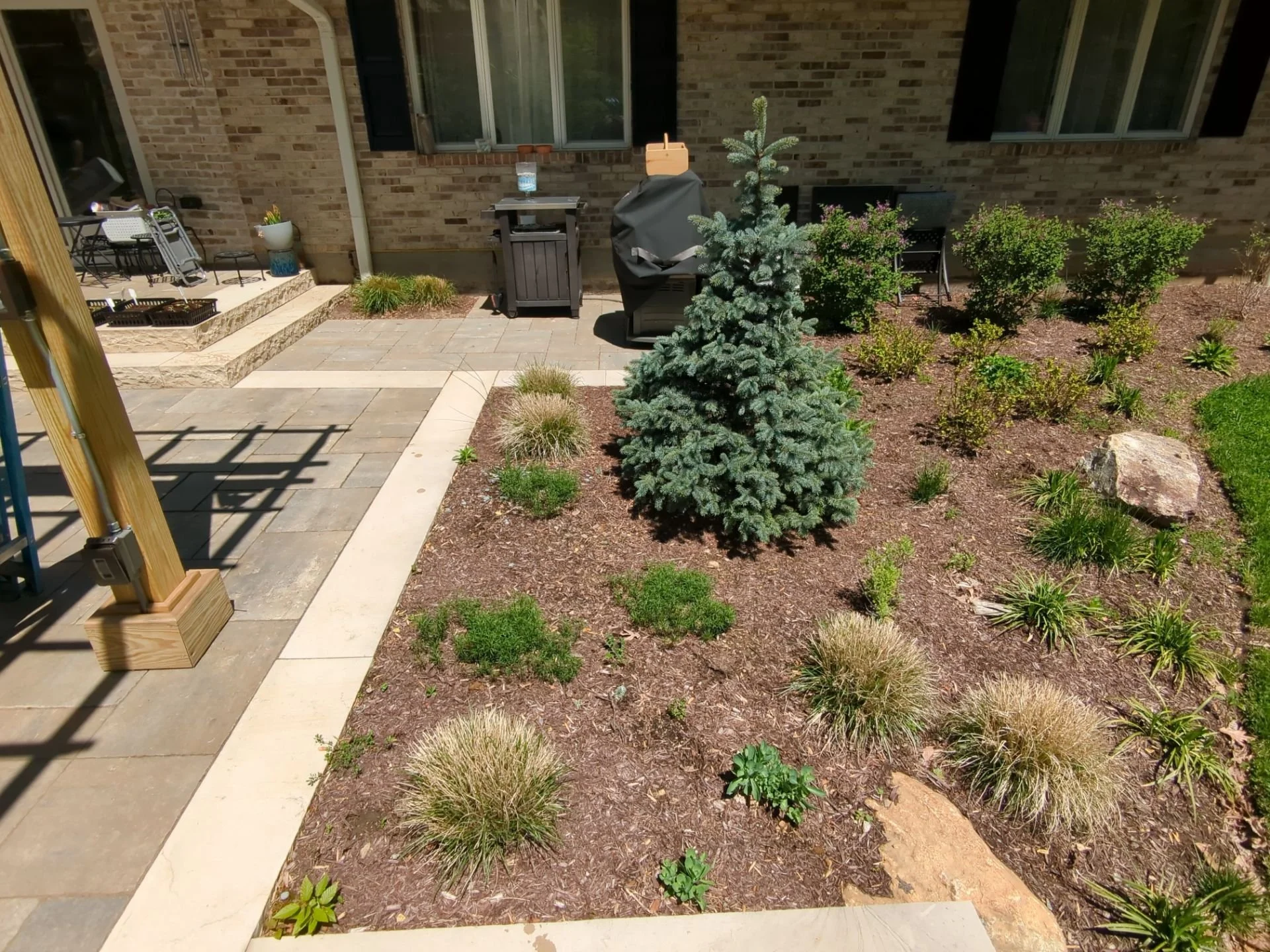 Landscaped patio with evergreen tree, ornamental grasses, perennial beds, stone walkway, and outdoor living area