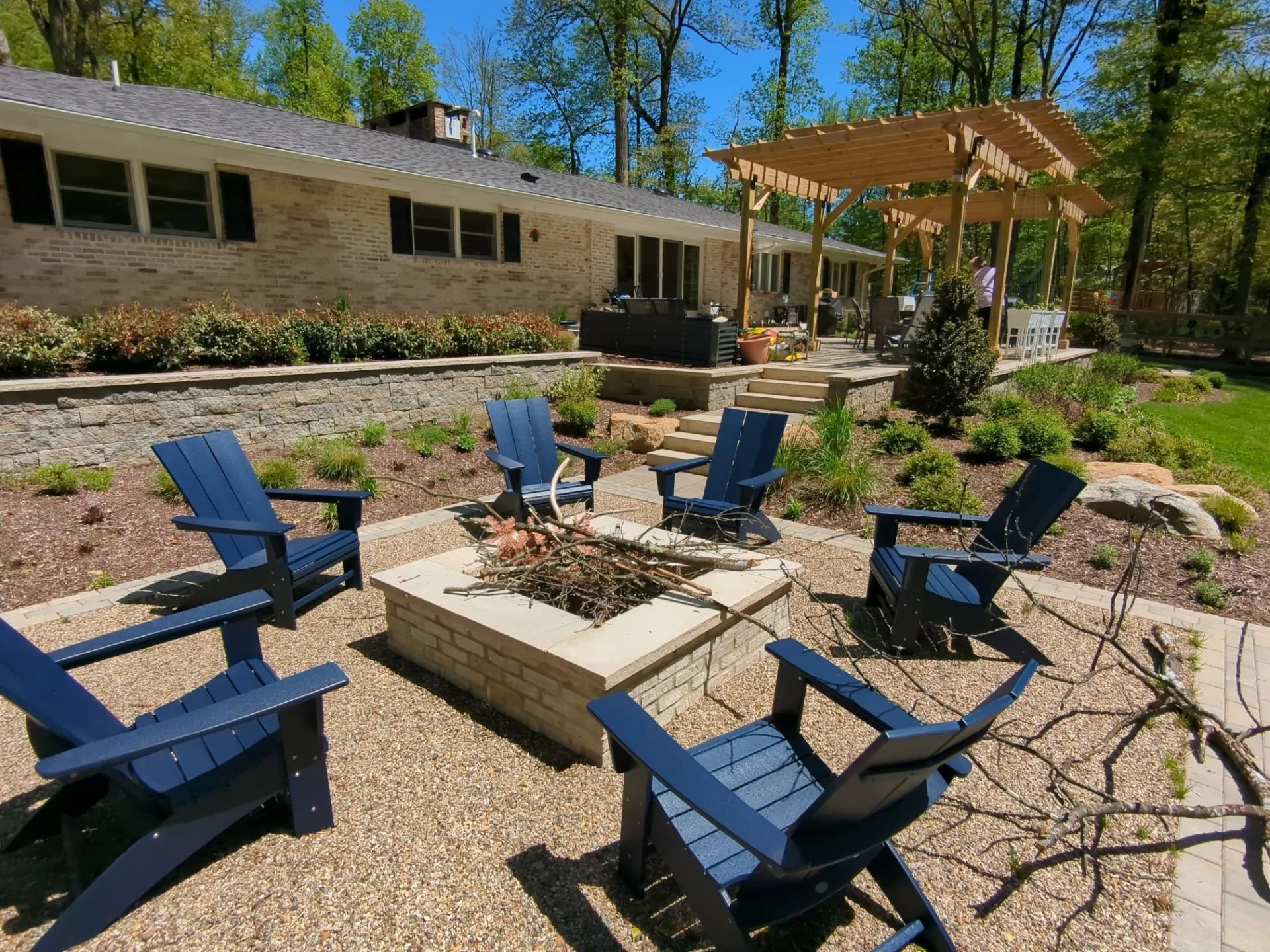 Wooden pergola, stone patio, layered perennial gardens, and lawn surrounding the home