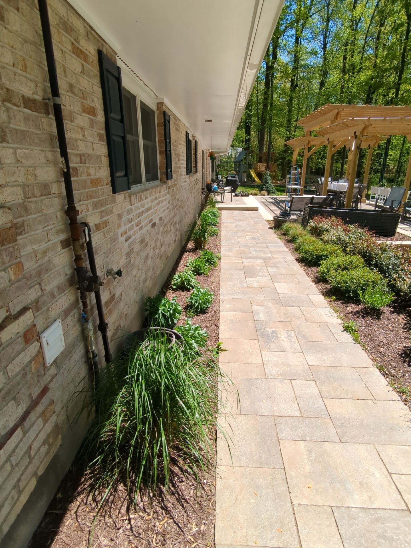 Stone paver walkway bordered by layered garden beds, ornamental grasses, and shrubs leading to a backyard pergola
