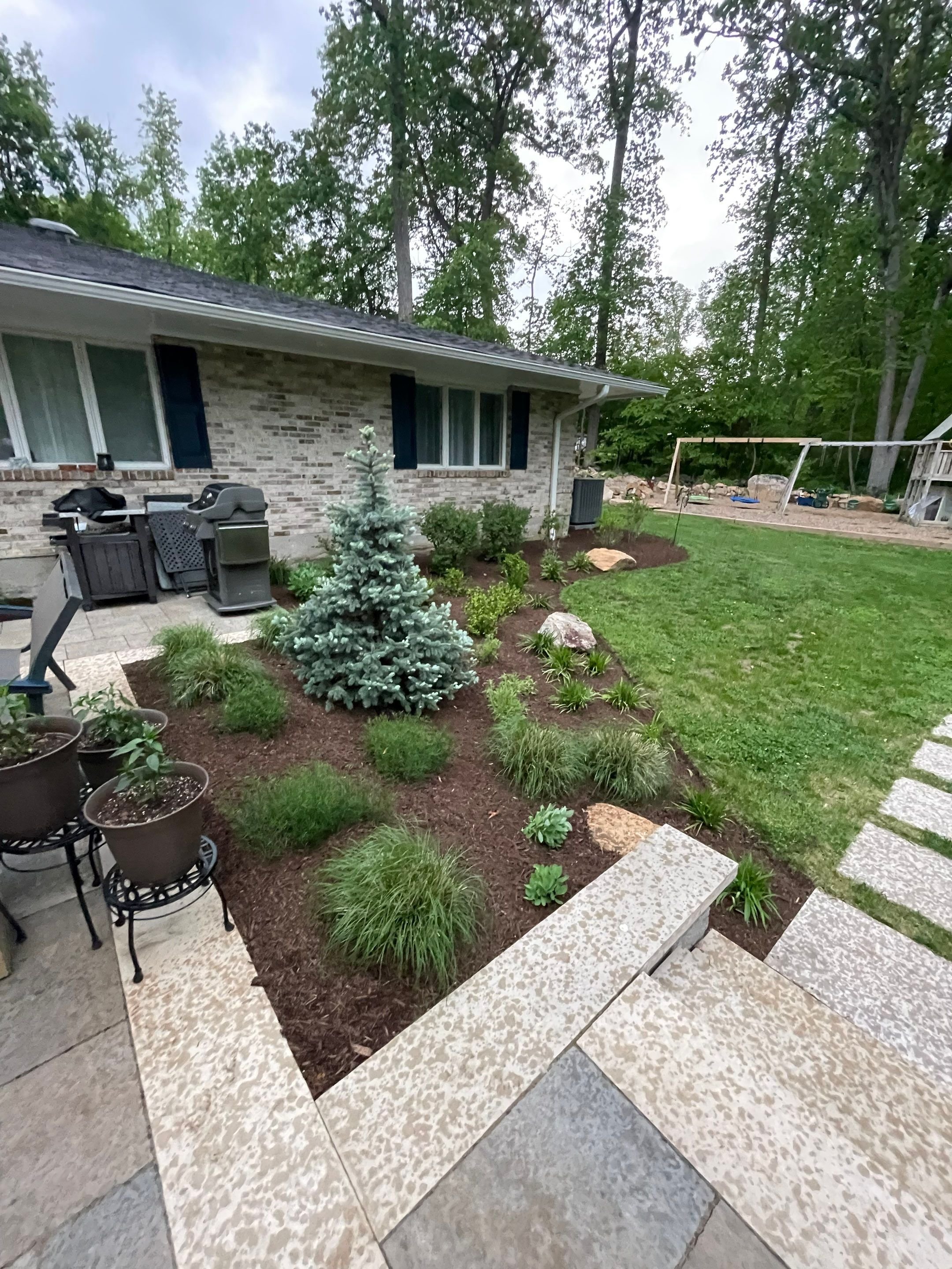 Perennial garden beds, ornamental grasses, evergreen tree, and stone walkway