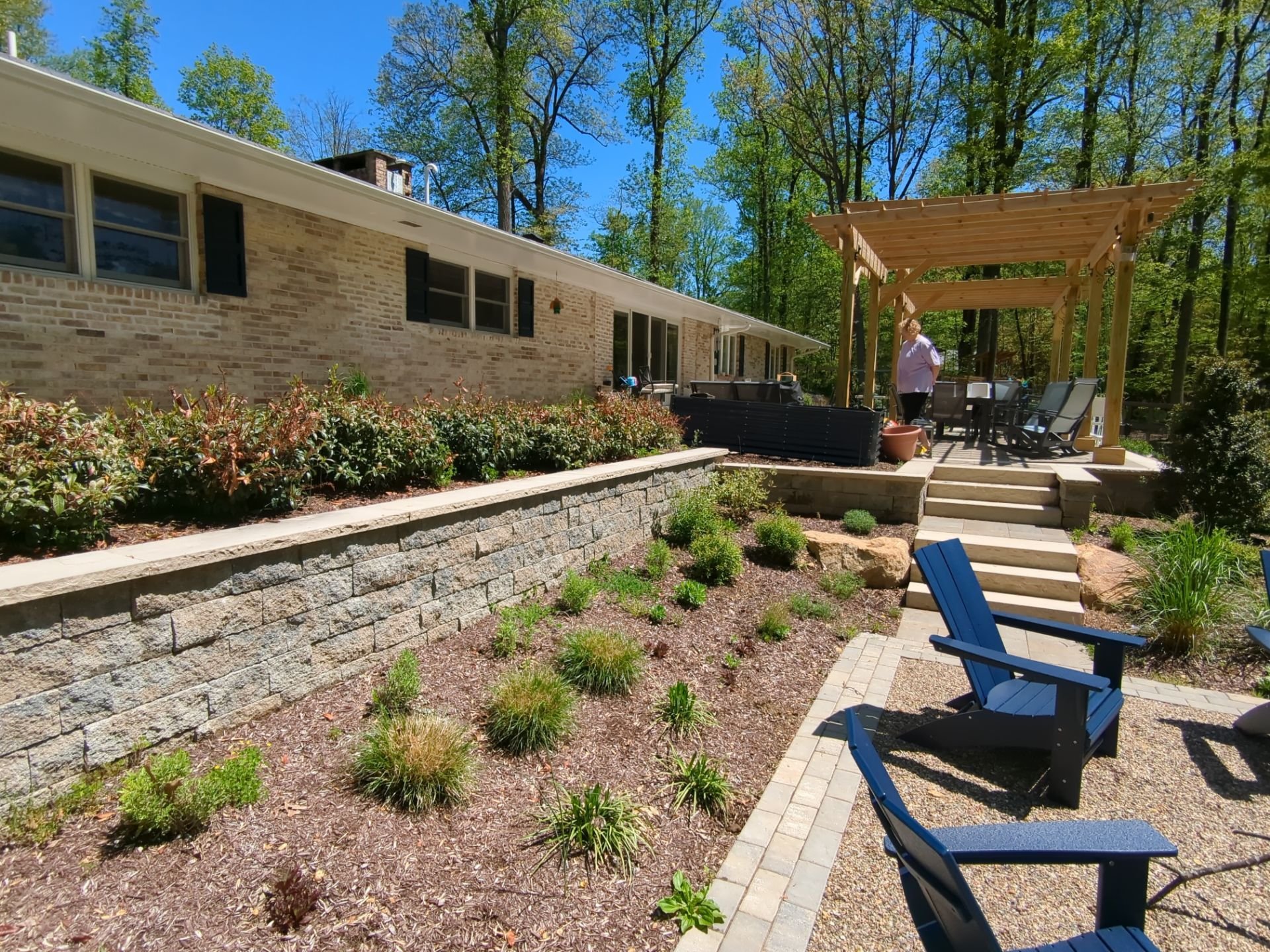 Backyard with pergola, stone retaining walls, garden beds, fire pit patio, and outdoor seating