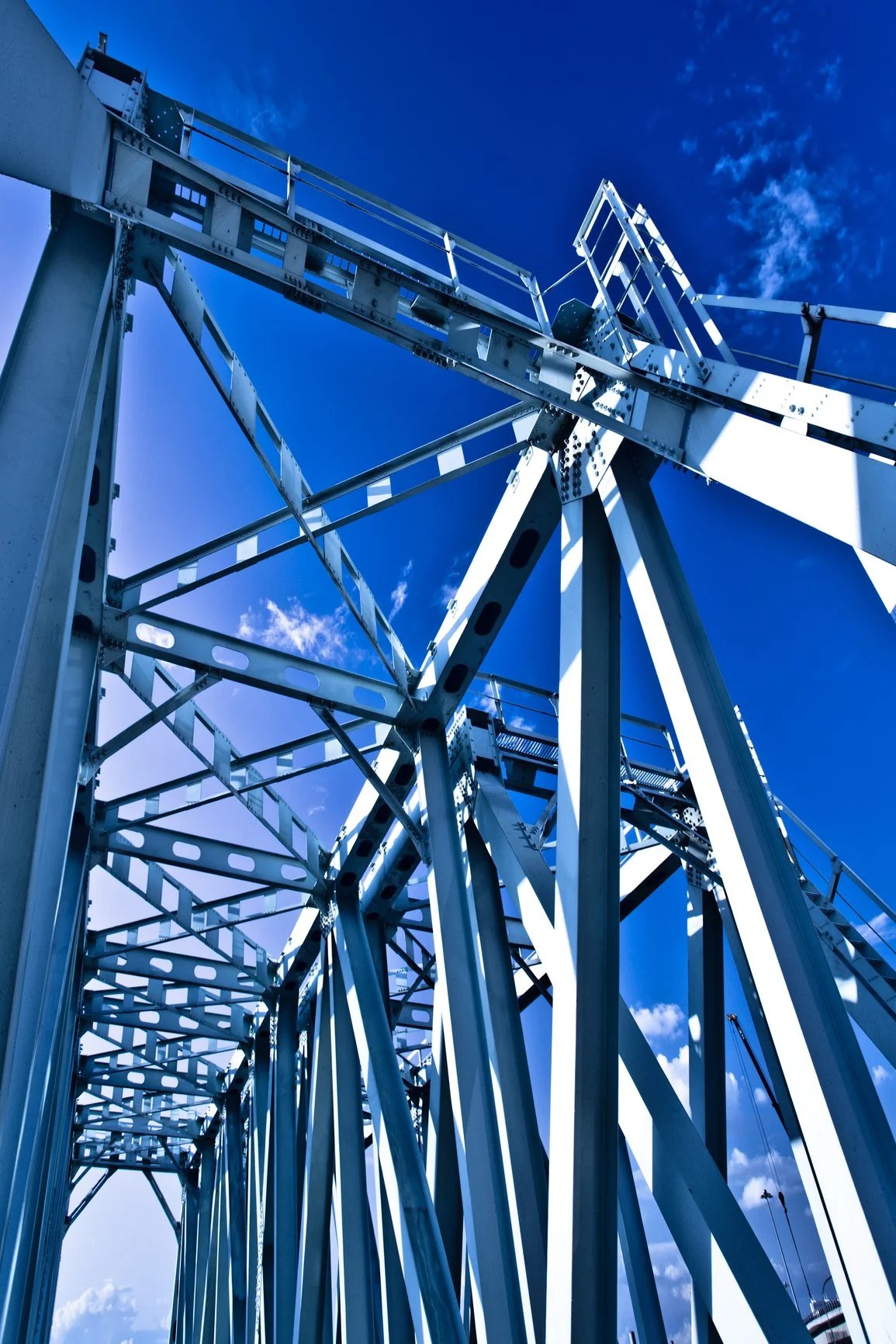 A close-up view of a metal Ferris wheel structure with blue sky and a few clouds in the background.