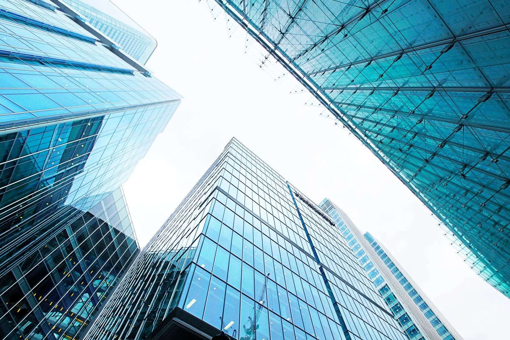 Looking up at modern glass skyscrapers with reflective windows in an urban cityscape against a cloudy sky.