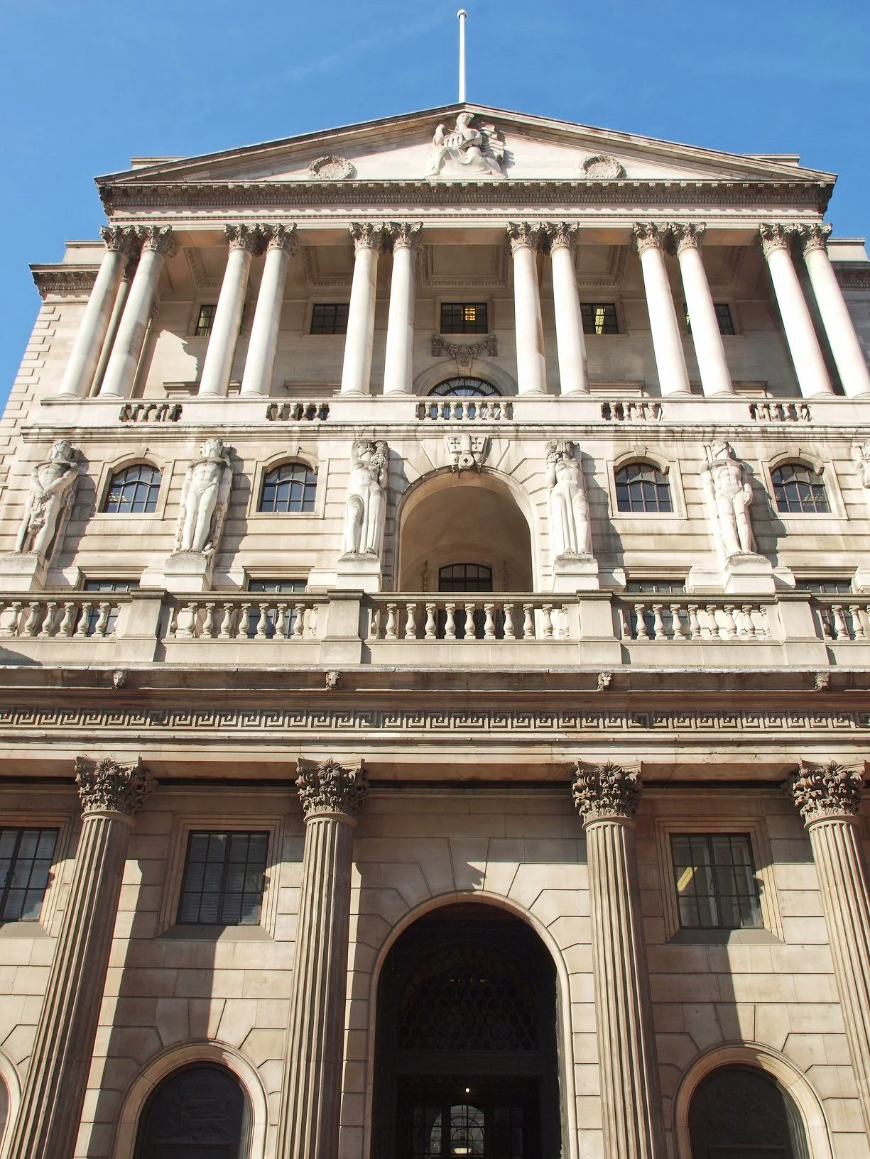 Facade of a neoclassical government building with large columns, statues, and decorative stonework, under a clear blue sky.