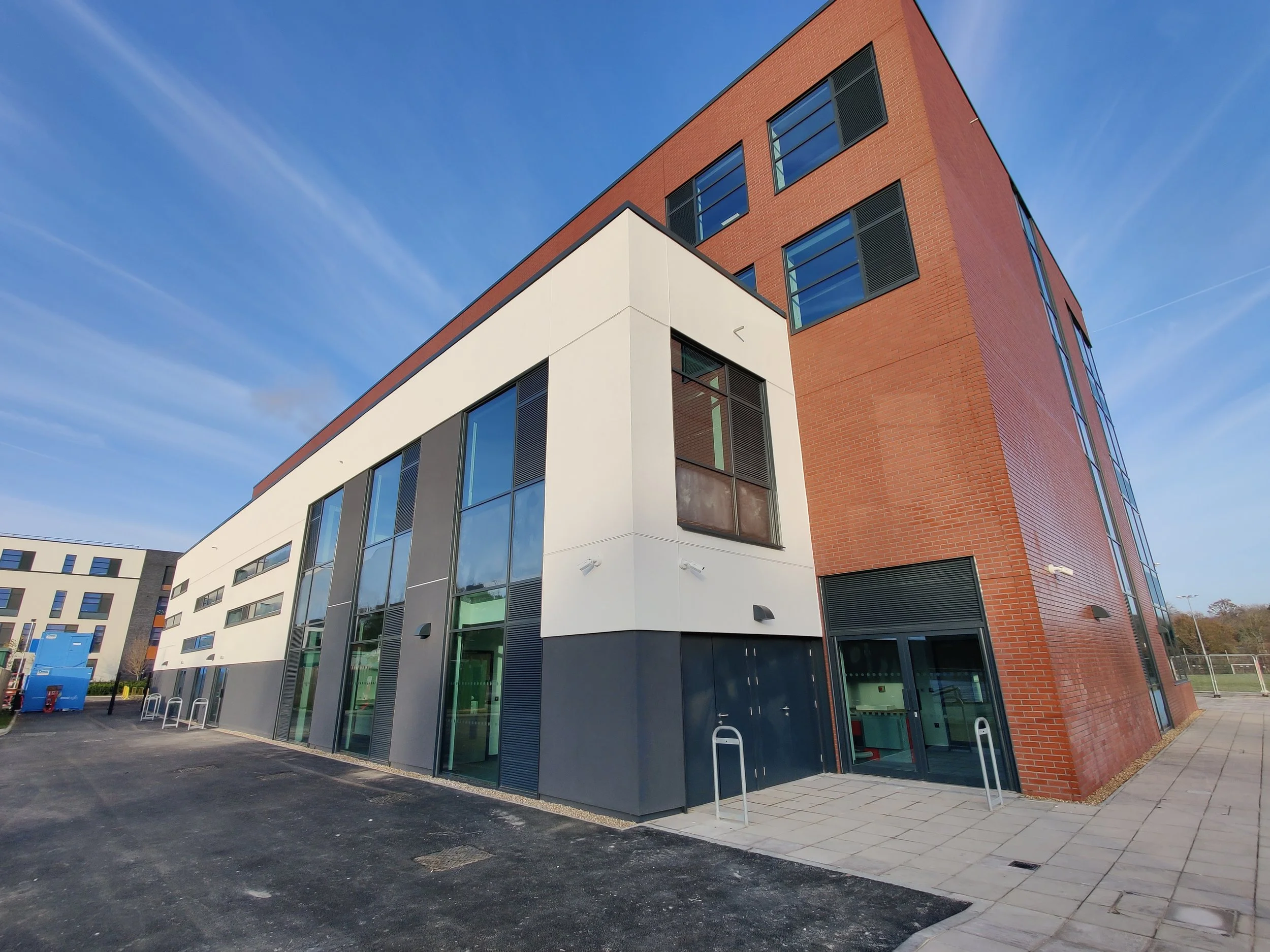 Low-angle view of a modern multi-story building with brick and glass facade against a blue sky.