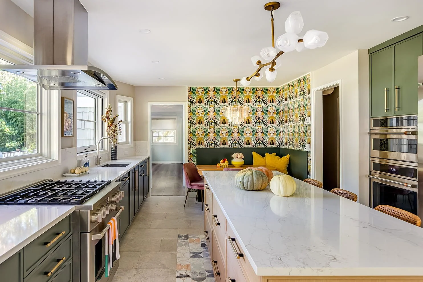 Open-concept kitchen with green cabinetry, white marble countertops, modern appliances, a large island with pumpkins and fall decor, and a floral accent wall in the dining area.
