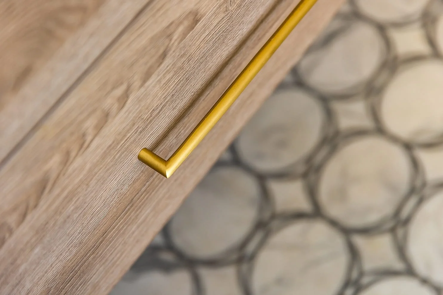 Close-up of a wooden cabinet with a gold handle, and a blurred background of circular patterned tiles.
