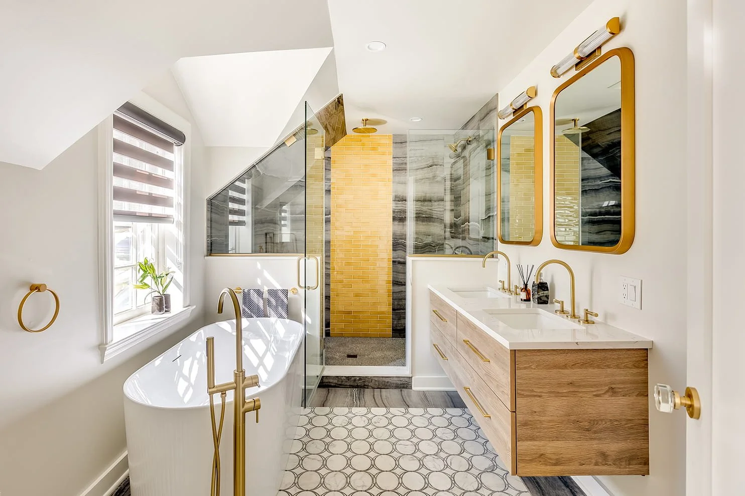 Modern bathroom with a large white soaking tub, double vanity with gold fixtures, and a glass-enclosed shower with a yellow brick accent wall.
