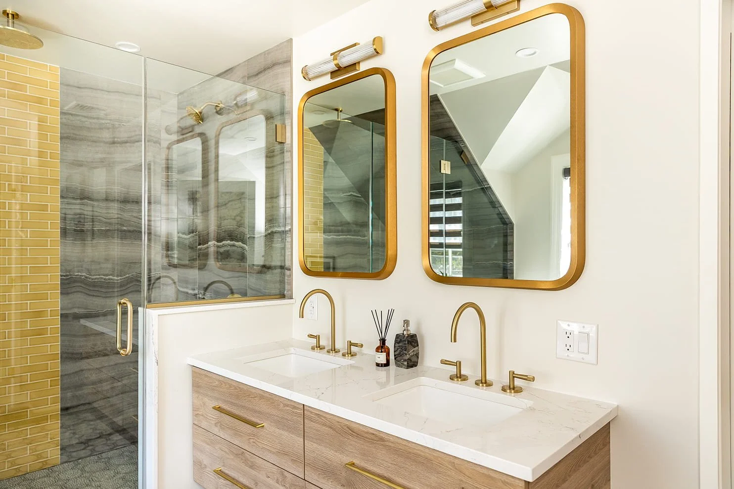 Modern bathroom with double vanity, gold fixtures, mirrors, and a walk-in shower with yellow brick and gray marble tiles.