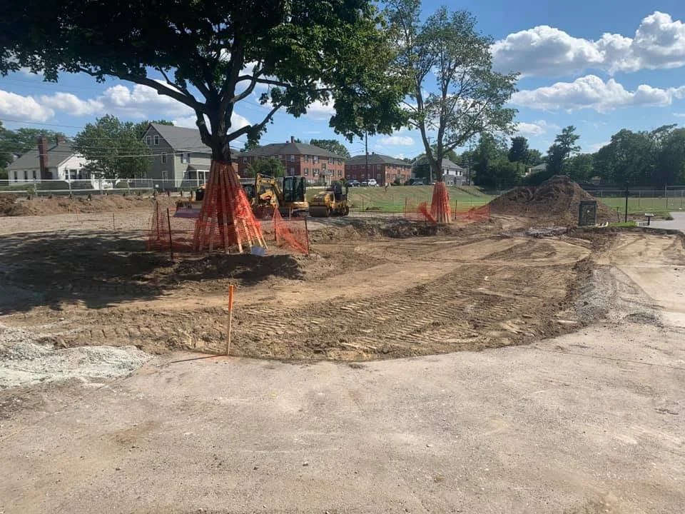Trees are roped off with orange fencing to ensure they are saved during a demolition and site work for a new playground install.