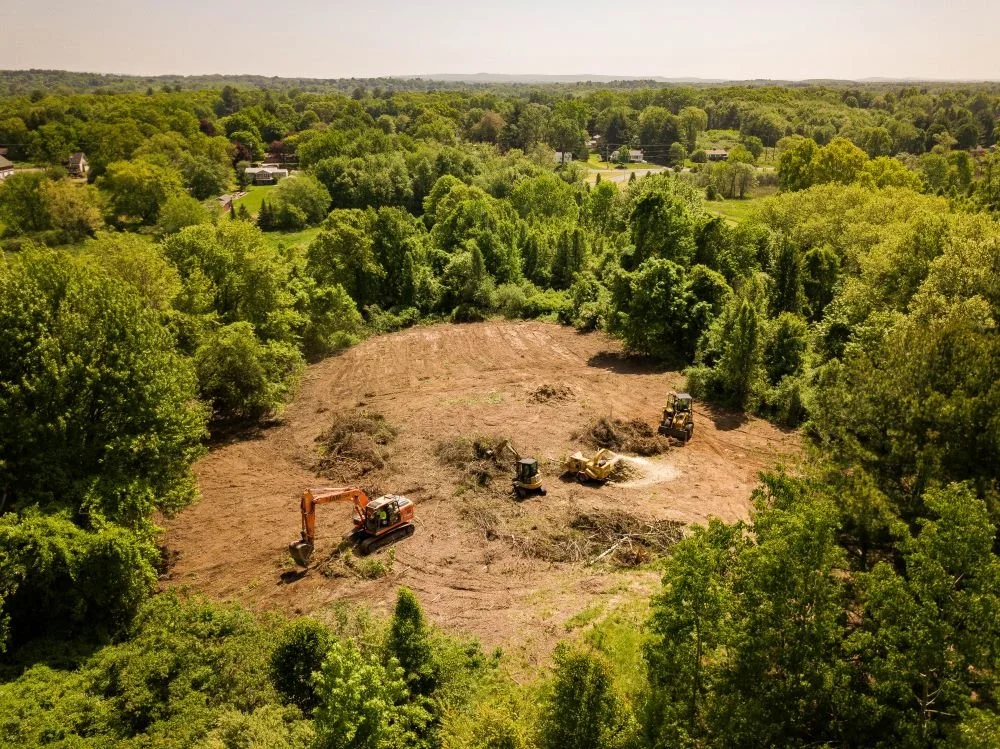 An aerial shot of the clearing of land where an excavator is working on preparing the site for a Dog Park.