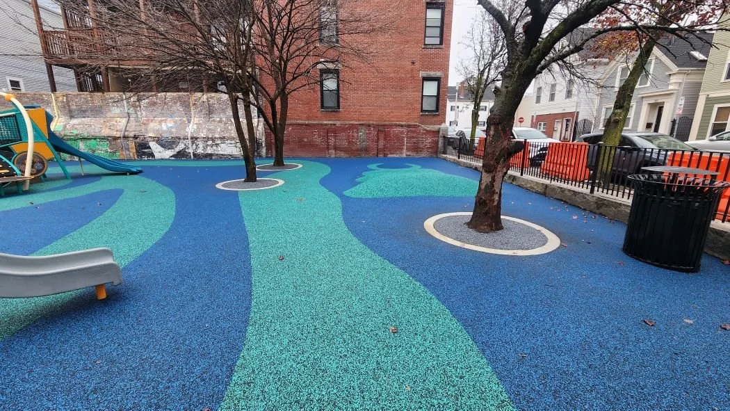 A view of the expertly installed rubber playground surfacing with slides and trees incorporated at Boston Public School 
