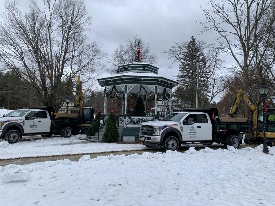 Two JAM Corporation trucks are parked on either side of the Gazebo in Townsend Common with snow covering the ground.