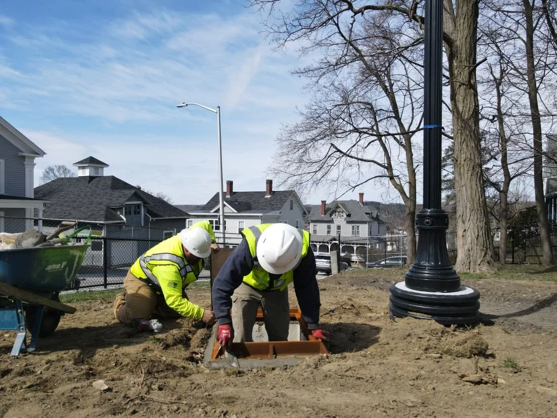 Two workers are working on the entrance to the underground utilities that have been installed for Grant Square Community Gardens.
