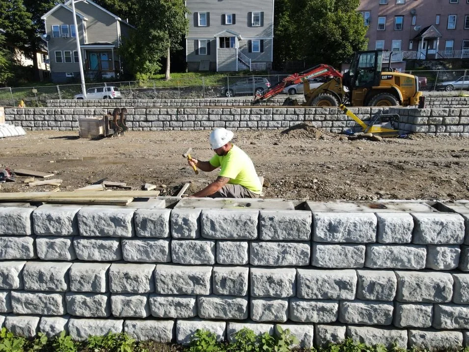 A stone retaining wall that is in progress with a worker kneeling behind it.