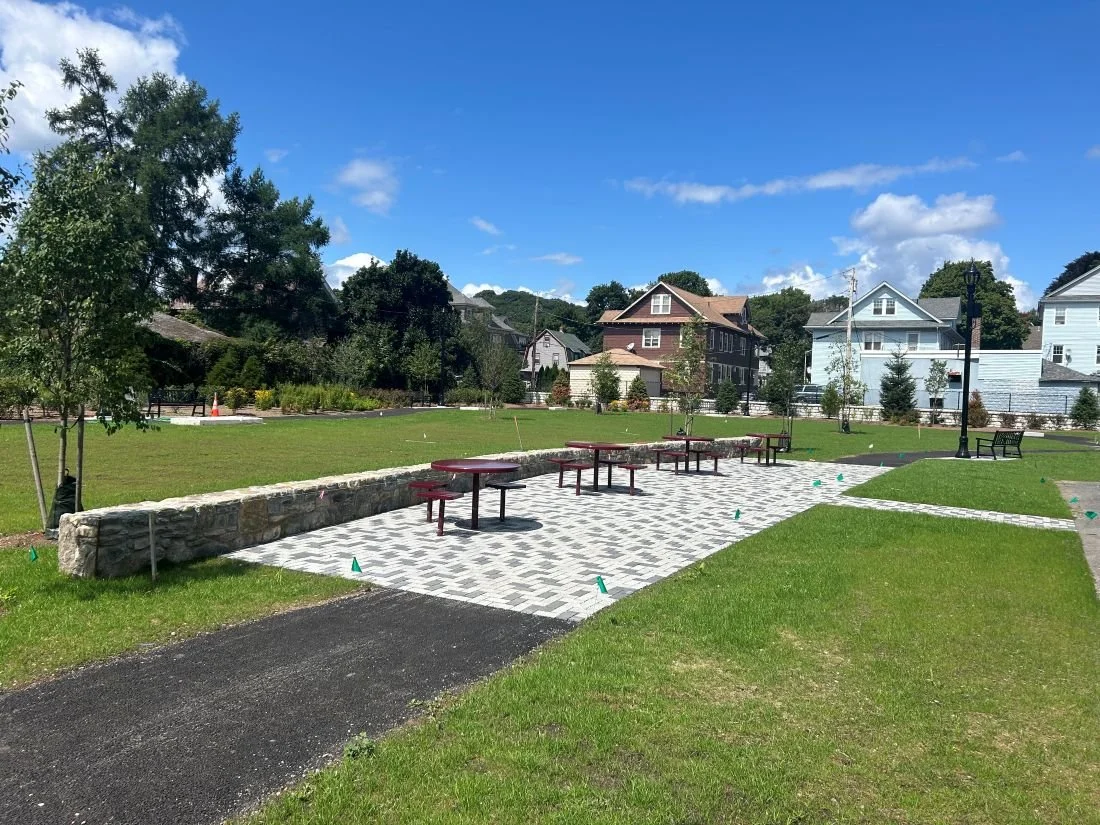 In Worcester Sever Street Park, new benches sit atop a stone paver patio with a stone wall behind it. 