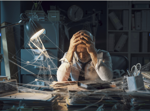 A man sitting at a cluttered desk with papers and files, holding his head in frustration, surrounded by tangled strings and a harsh desk lamp.