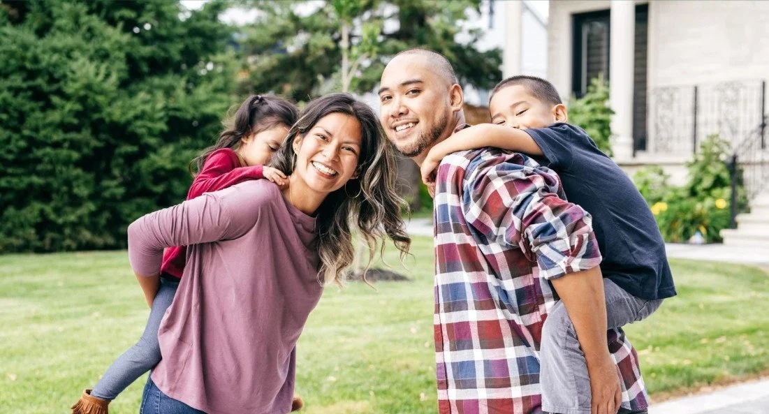 Family outdoors, woman smiling, man carrying a child on his back