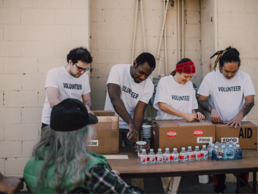 A group of volunteers working together at a community service event, packing food and water bottles at a table.