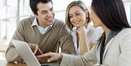 Three people sitting at a table looking at a tablet and smiling.