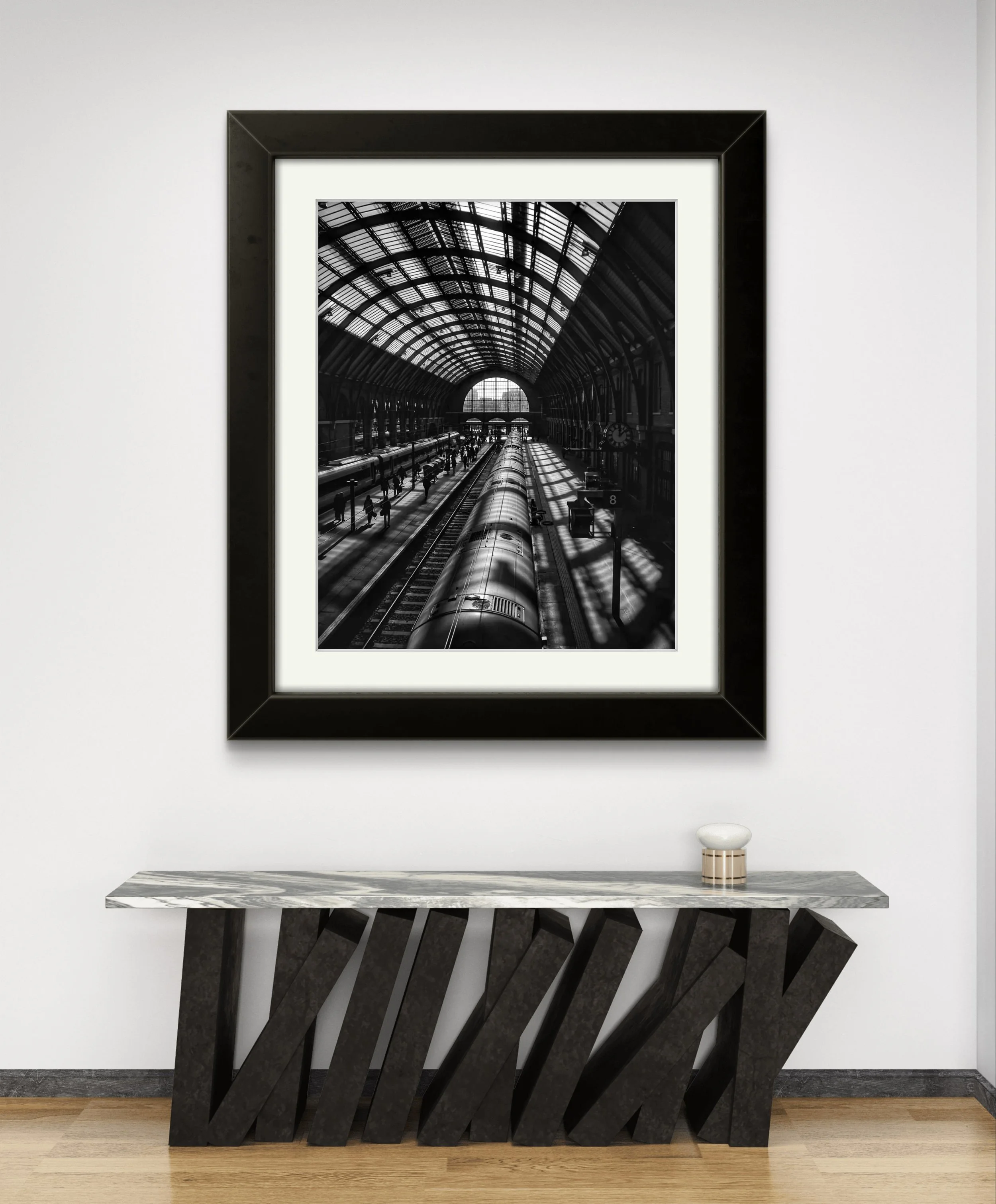 Photographie en noir et blanc de la gare de King's à Londres, Verrière baignée de lumière et voyageurs sur le quai
