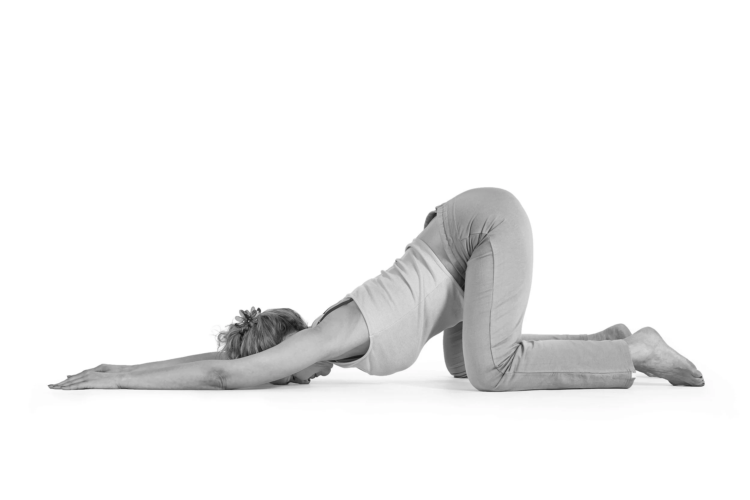 Femme faisant la posture de l'enfant en yoga, genoux pliés, bras tendus vers l'avant, tête au sol sur un fond blanc.