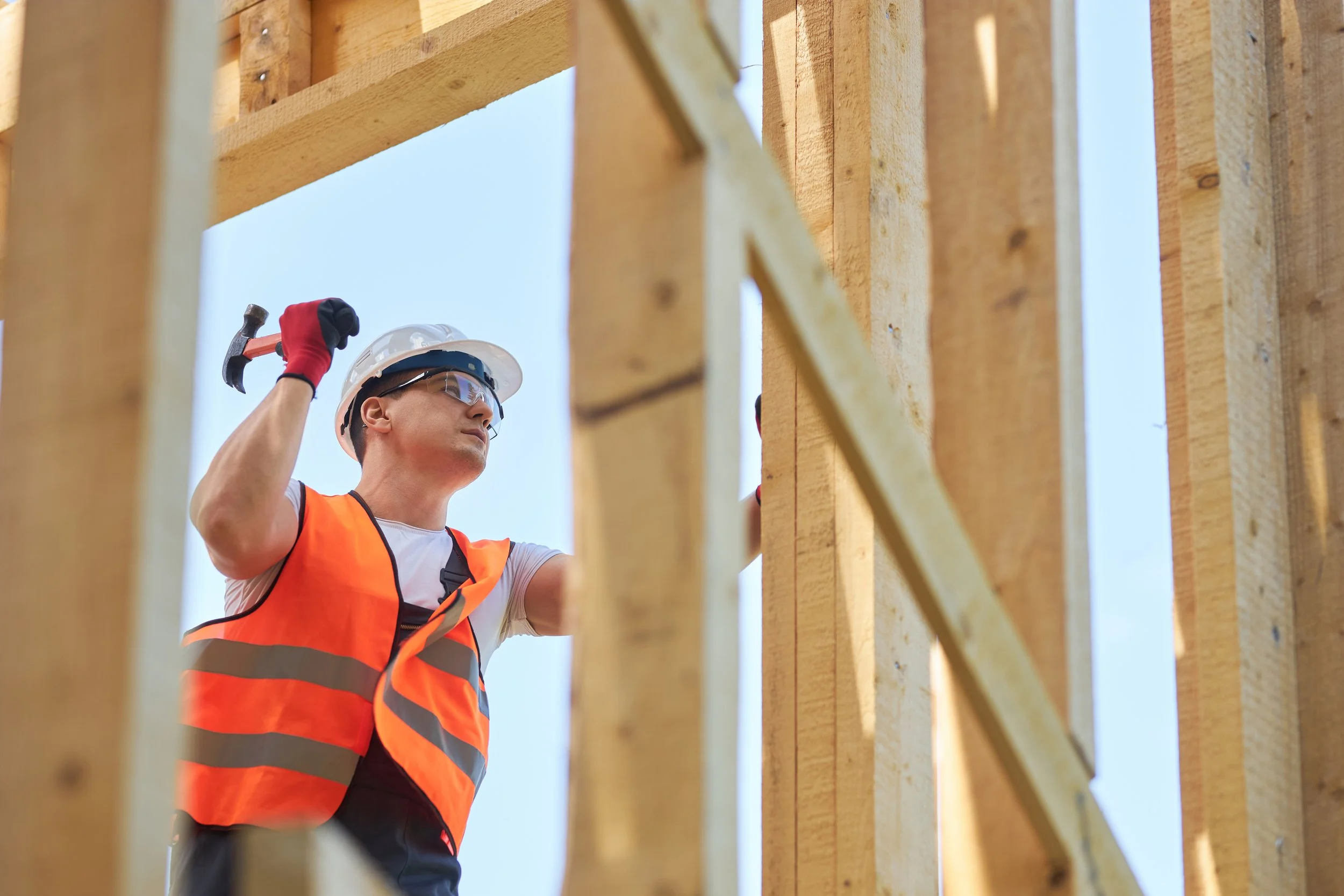 Construction worker in safety gear using a hammer on a wooden frame.