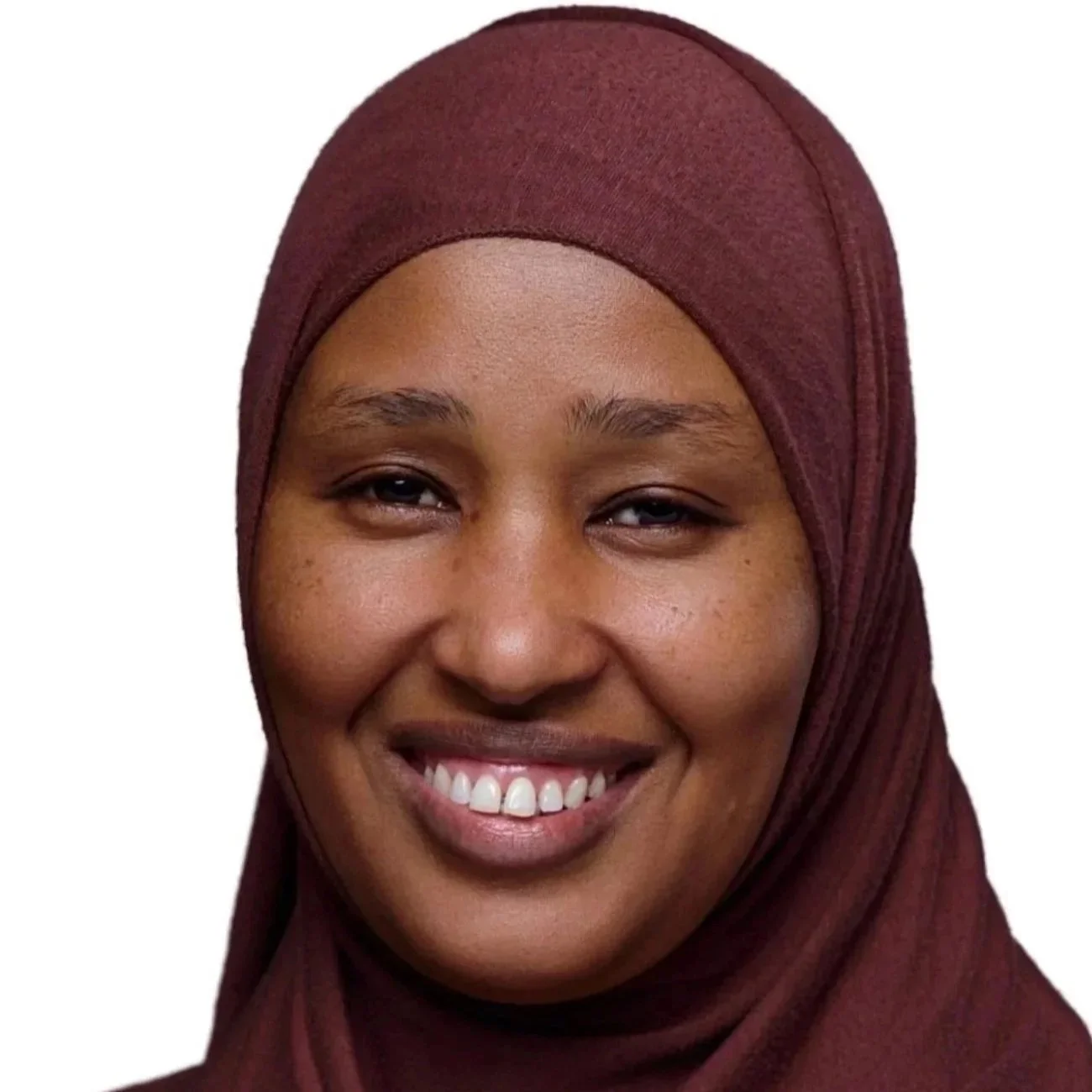 A woman wearing a maroon hijab smiling and speaking at a podium, with three other people standing in the background.