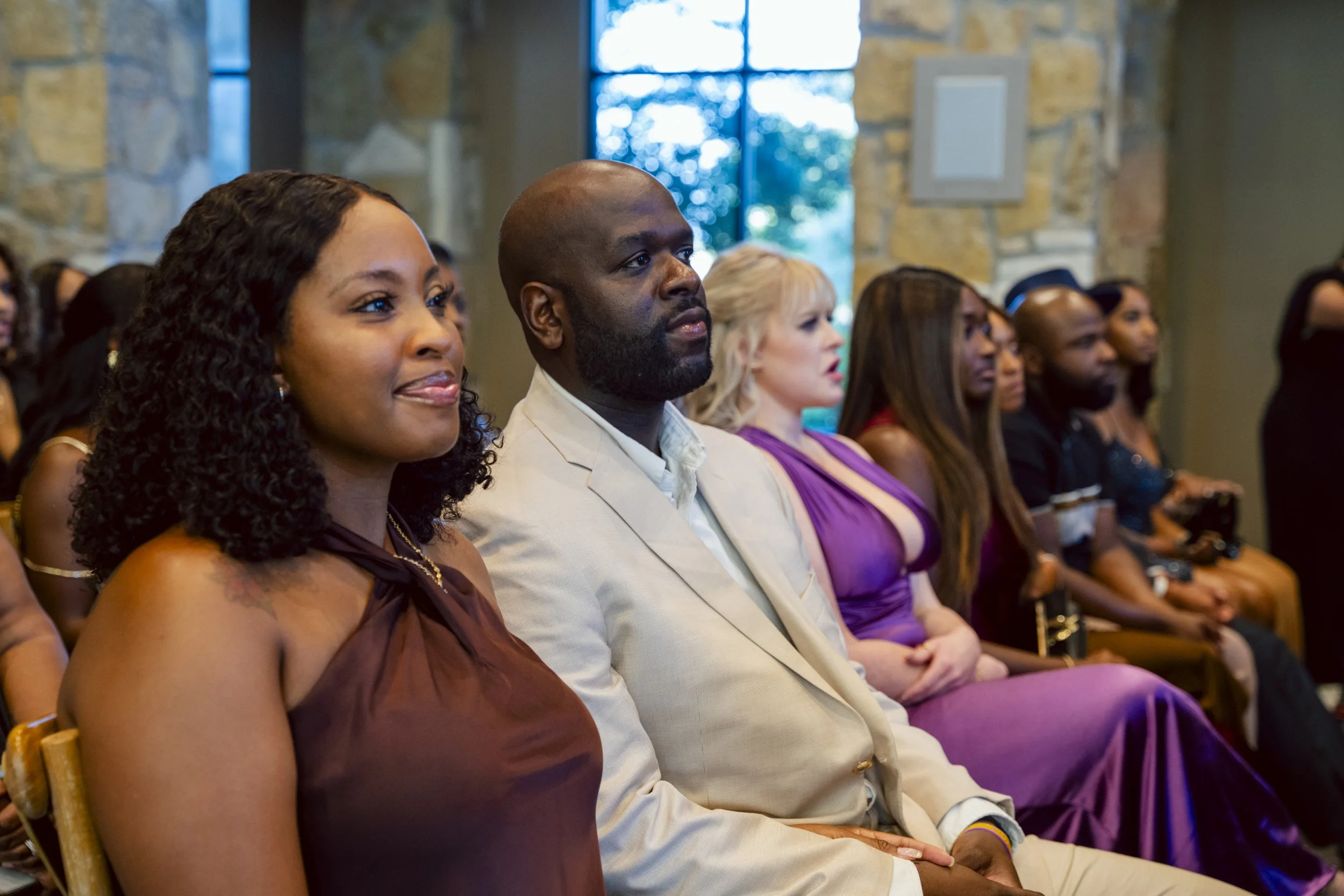 Attendees, including men and women, seated indoors at an event, listening attentively.