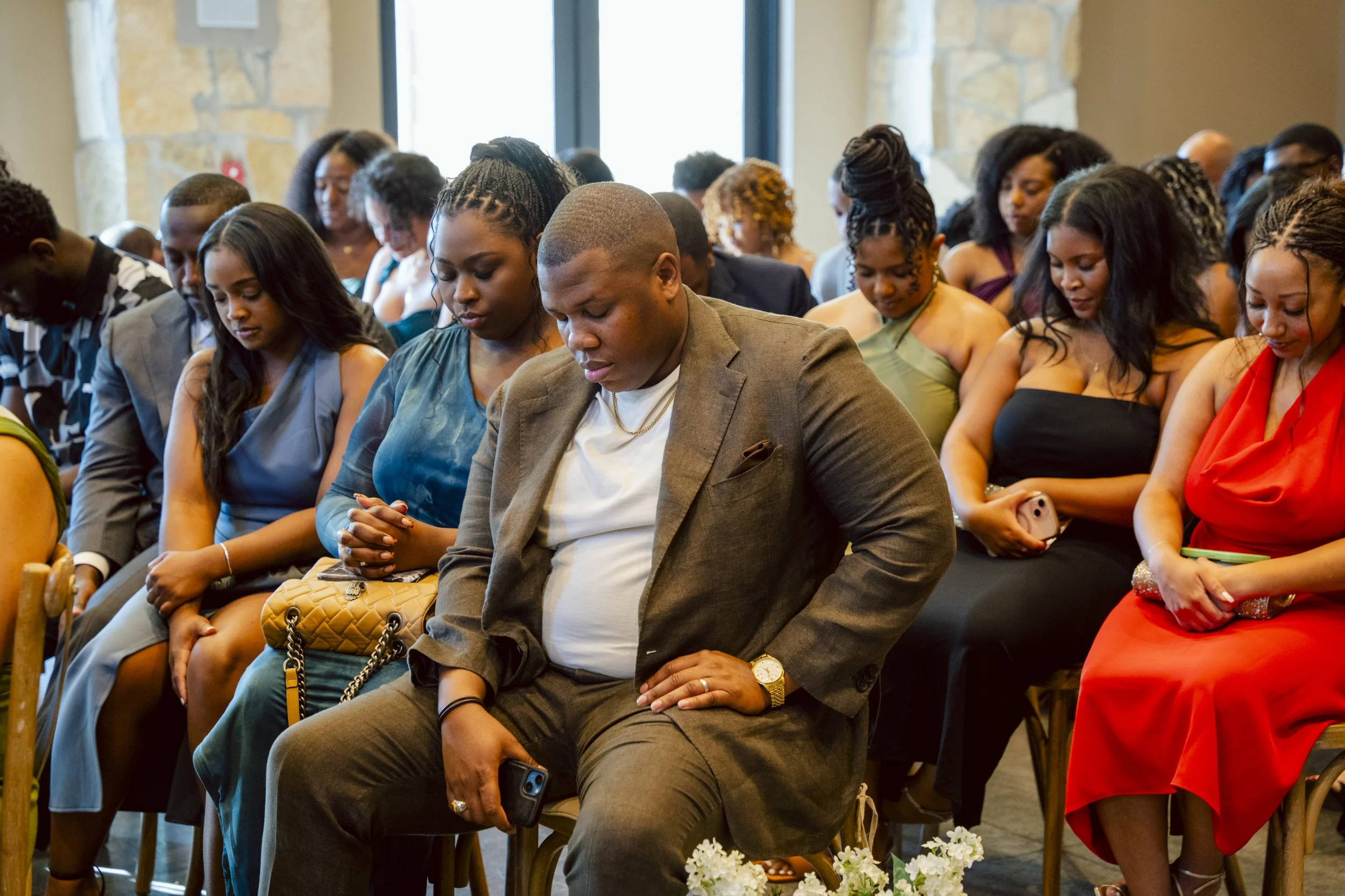 Group of people sitting with heads bowed and eyes closed during a prayer or moment of reflection in a church or event setting