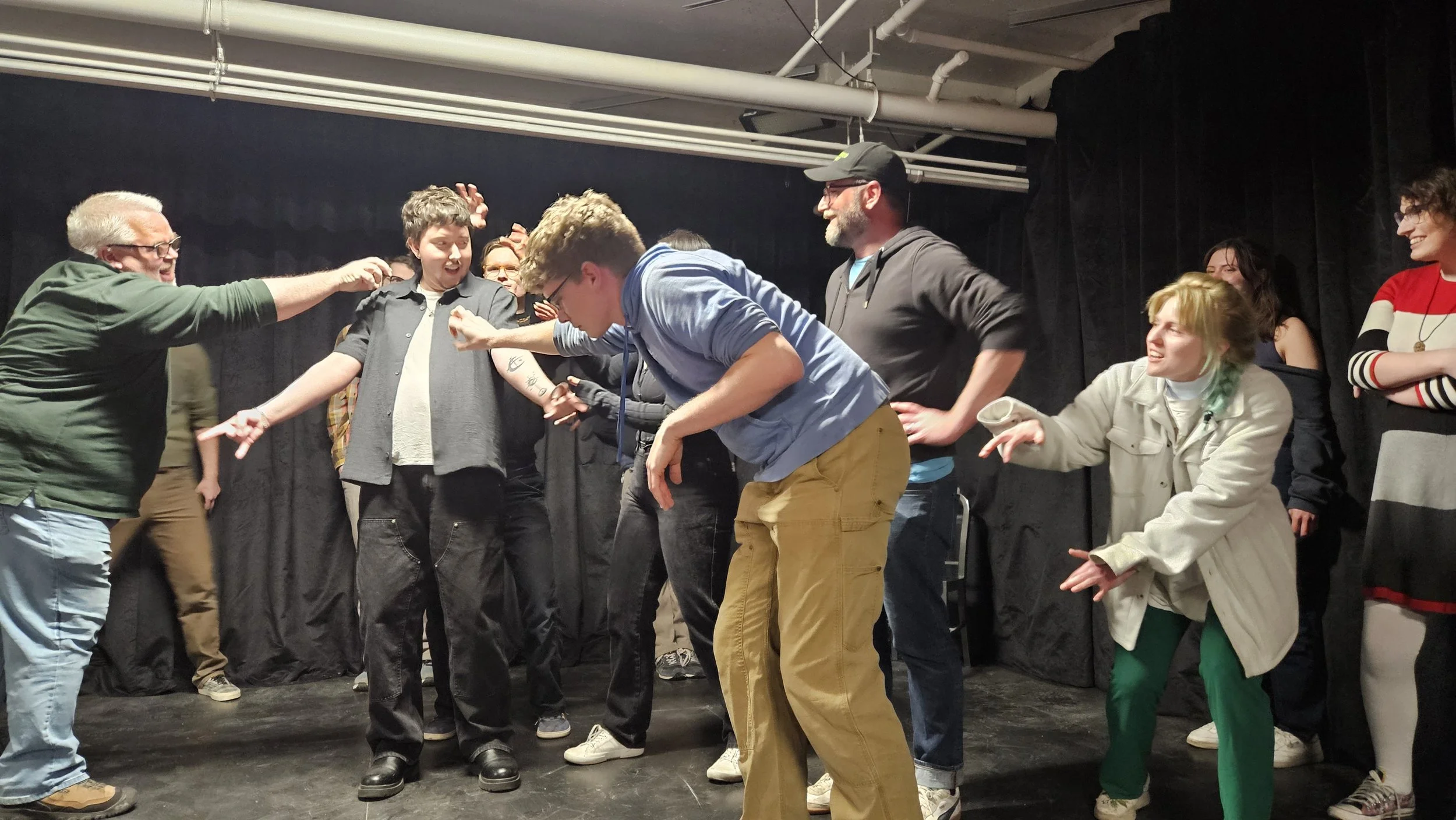 Photo of improvisers of all levels creating a stage picture of a character with creatures crawling over him, like something you'd see in DND!