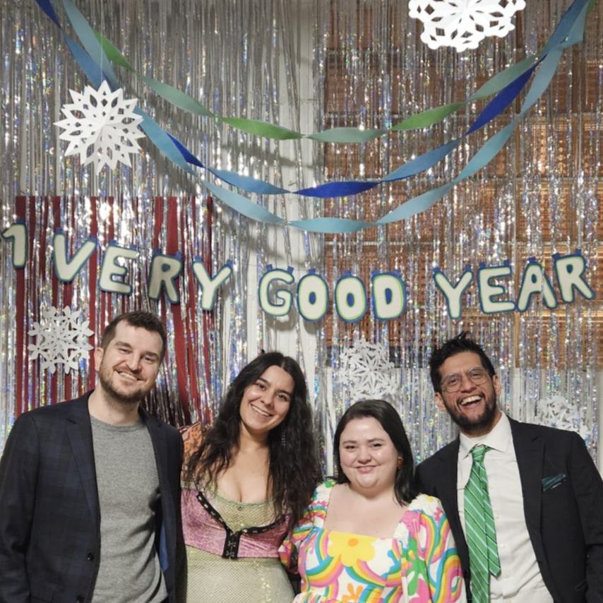 Image of the VGI Founders from Left to Right, Bradley Machov, Steph Callaghan, Laura Berger, and Chris Rodriguez, wearing fancy clothes with a banner overhead that reads "1 Very Good Year". This was taken at the VGI Winter Formal Jam & Fundraiser.