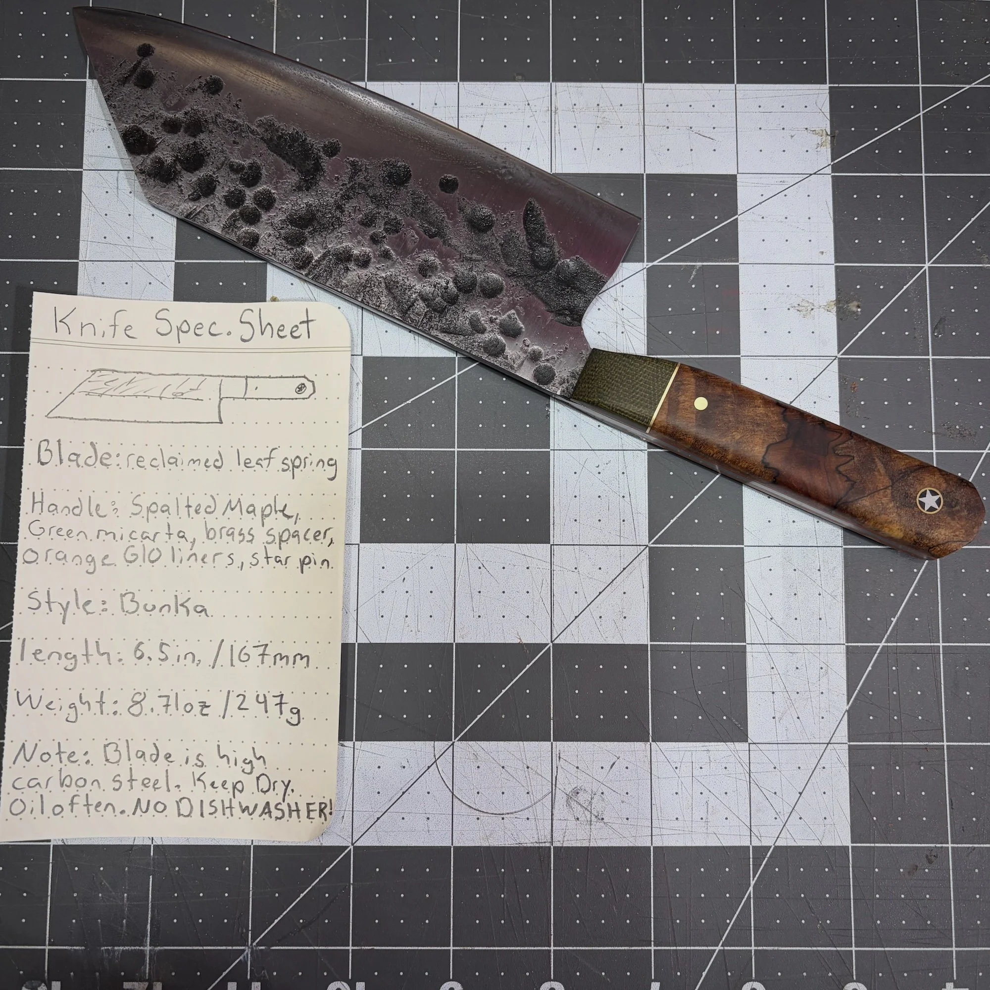 Handmade custom chef knife with a forged-texture blade and reddish-brown wood handle beside its handwritten design notes.