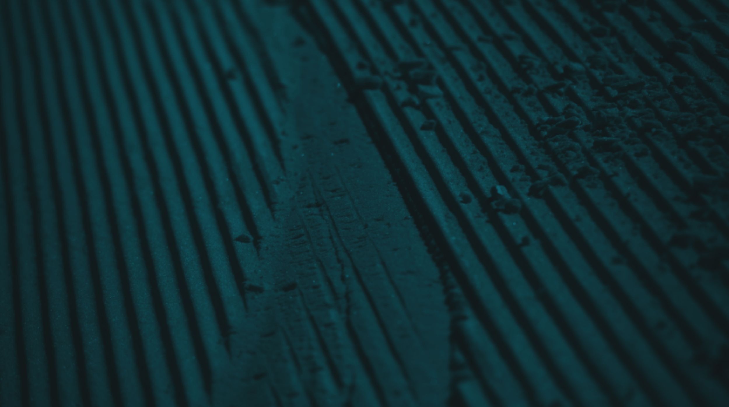 Close-up of textured metal surface with linear grooves, illuminated in blue-green light.