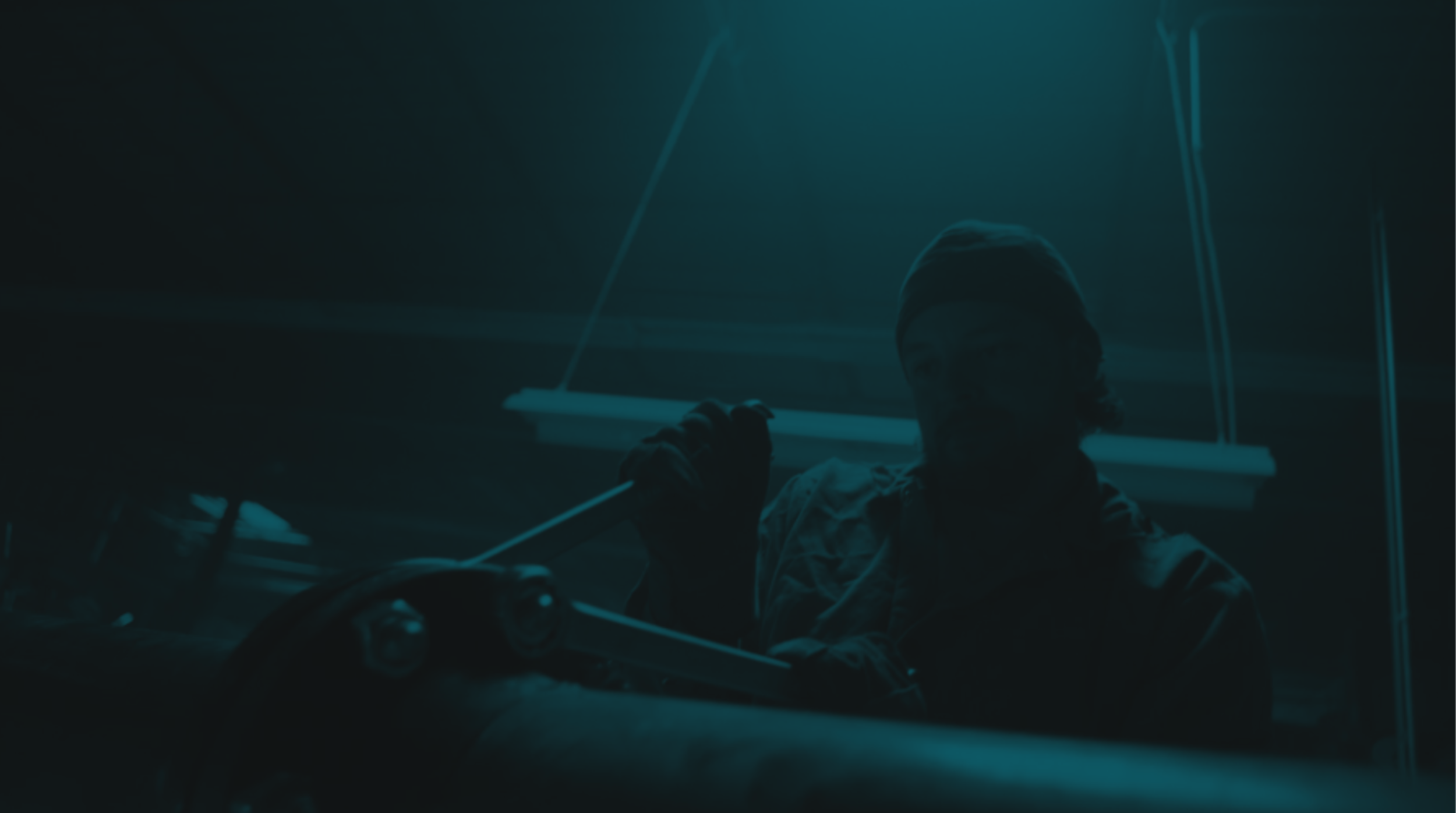 A person wearing a beanie sitting in a dimly lit space, holding a long object, with neon lights illuminating the background.