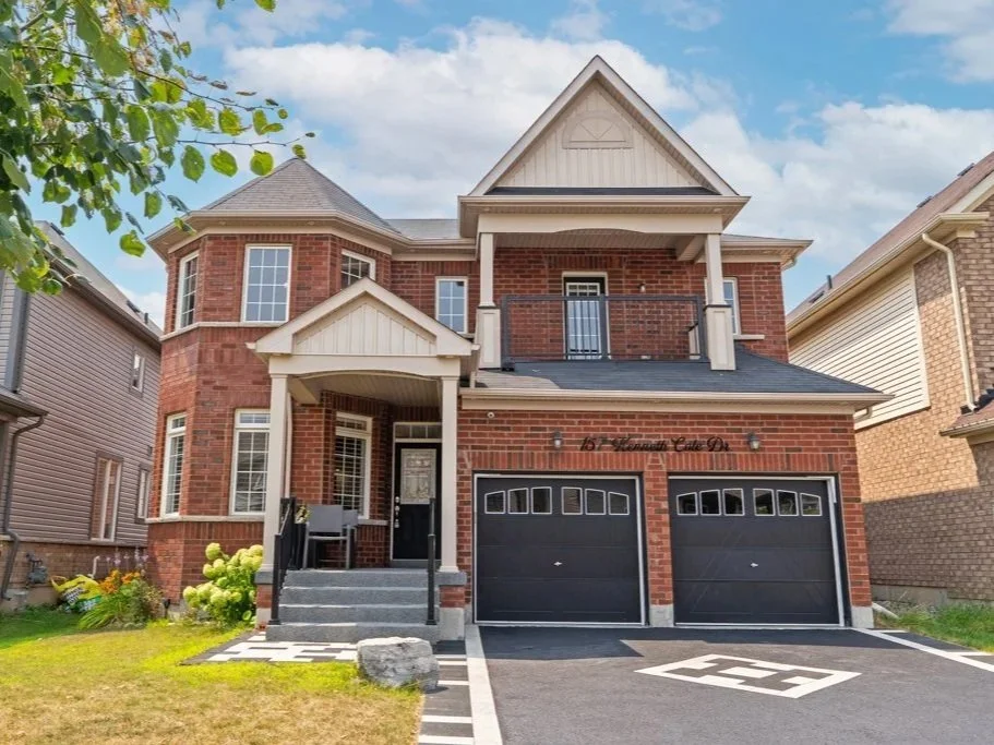Two-story brick house with a modern front porch, a black double garage door, and a small balcony on the second floor, under a blue sky with some clouds.