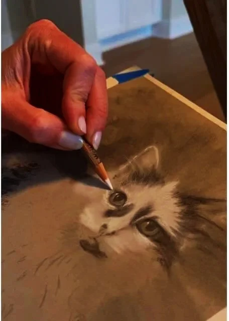 Close-up of an artist's hand using a fine-tip pencil to create a realistic drawing of a cat's face on brown paper.