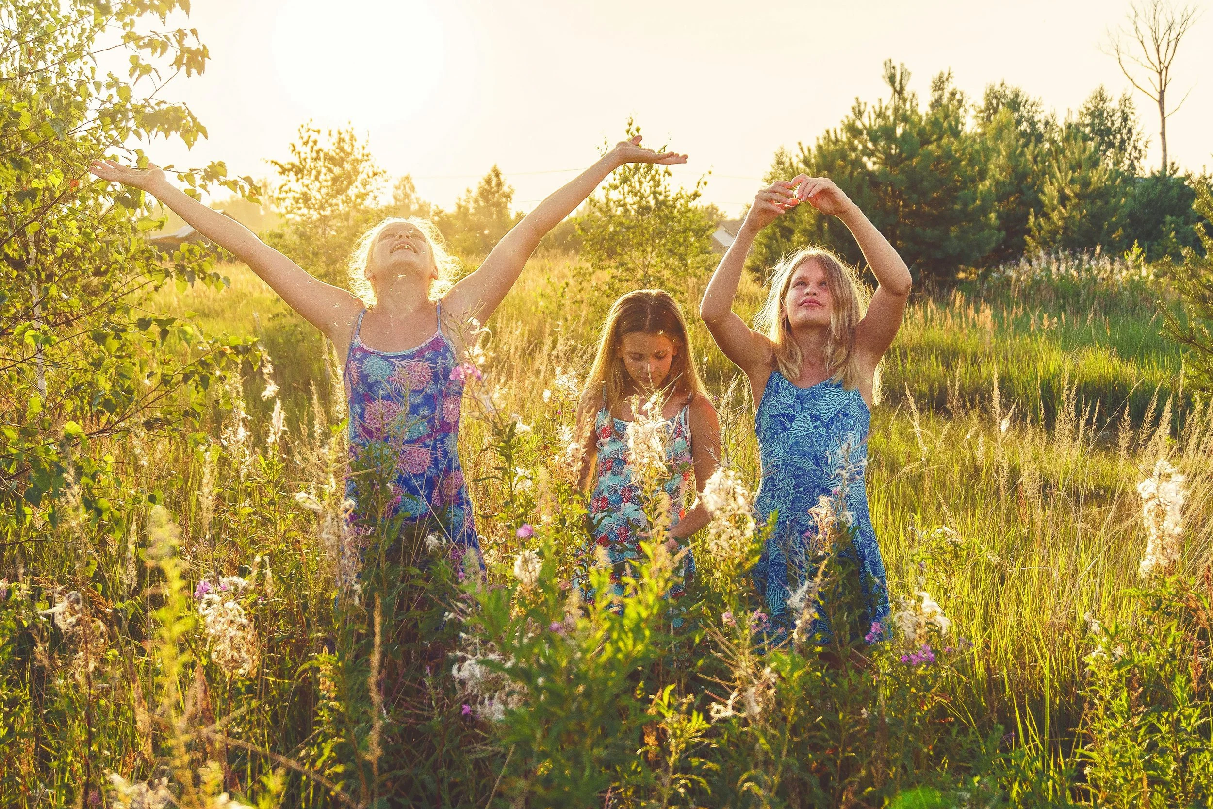 Girls in floral dresses celebrating wellbeing together in a sunny green field