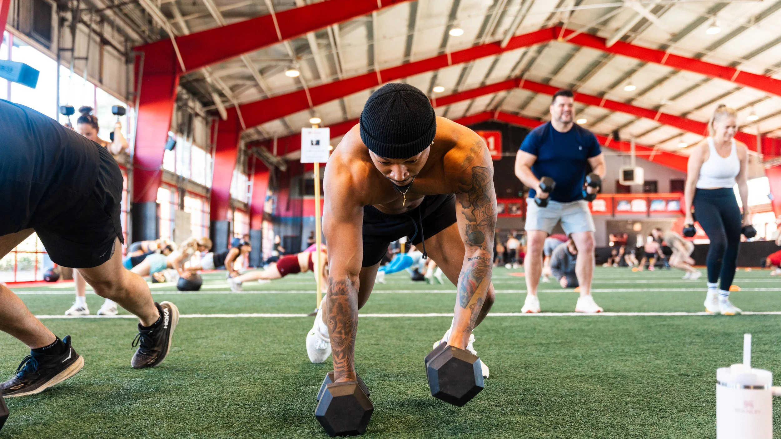 A man doing a HIIT workout with dumbbells on the ground in a gym with other people exercising in the background.