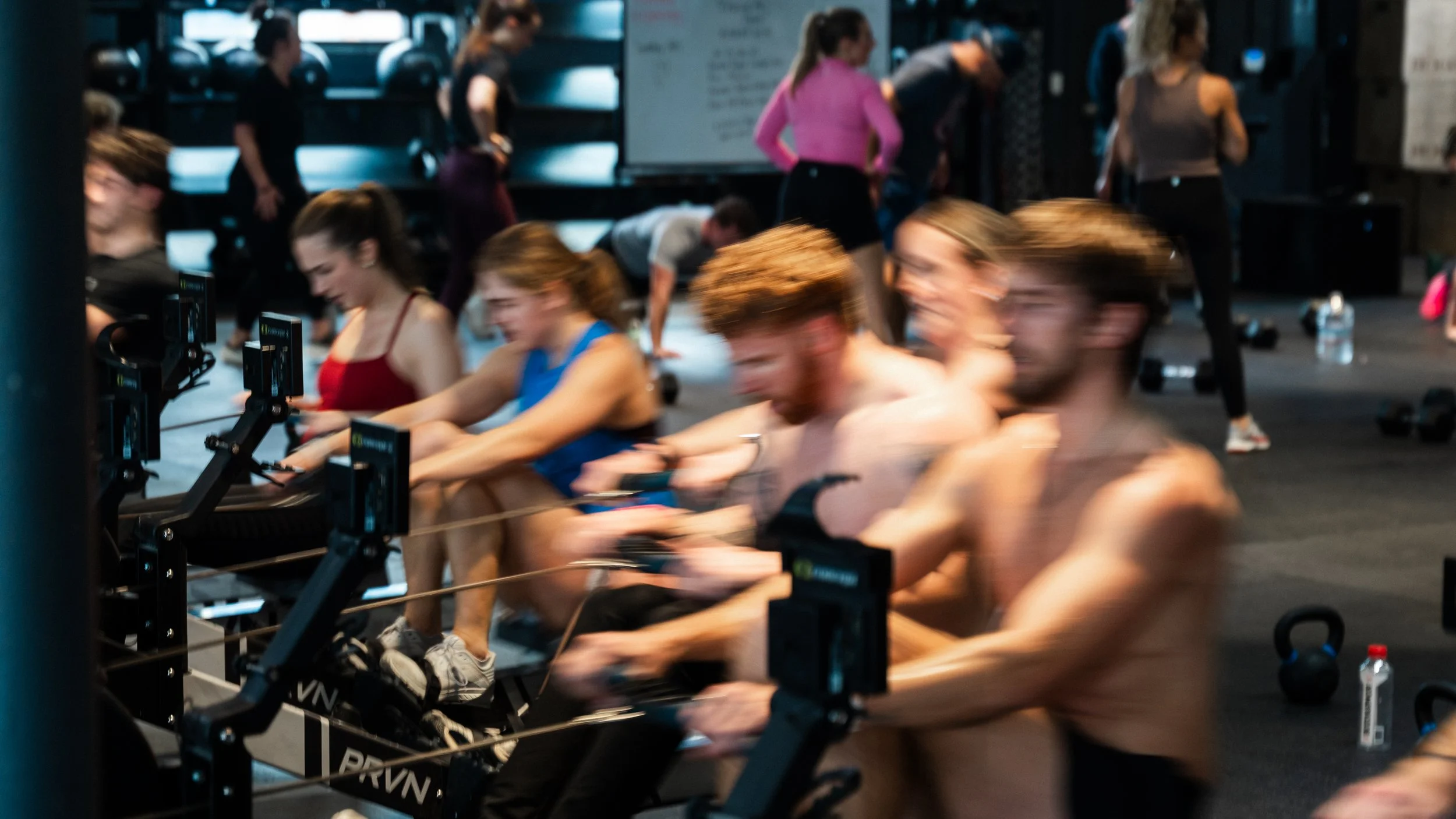 People participating in a spin class or indoor cycling workout in a gym, with some individuals riding stationary bikes and others standing or preparing to ride.