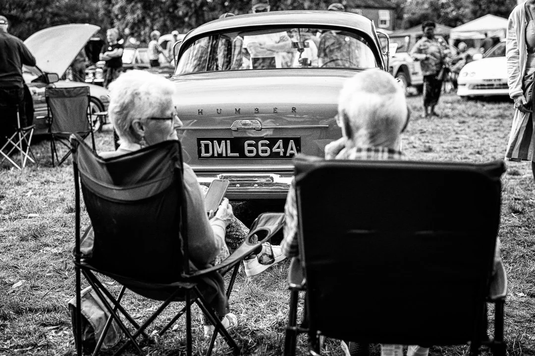 Two senior people sit by their classic car on show.jpg