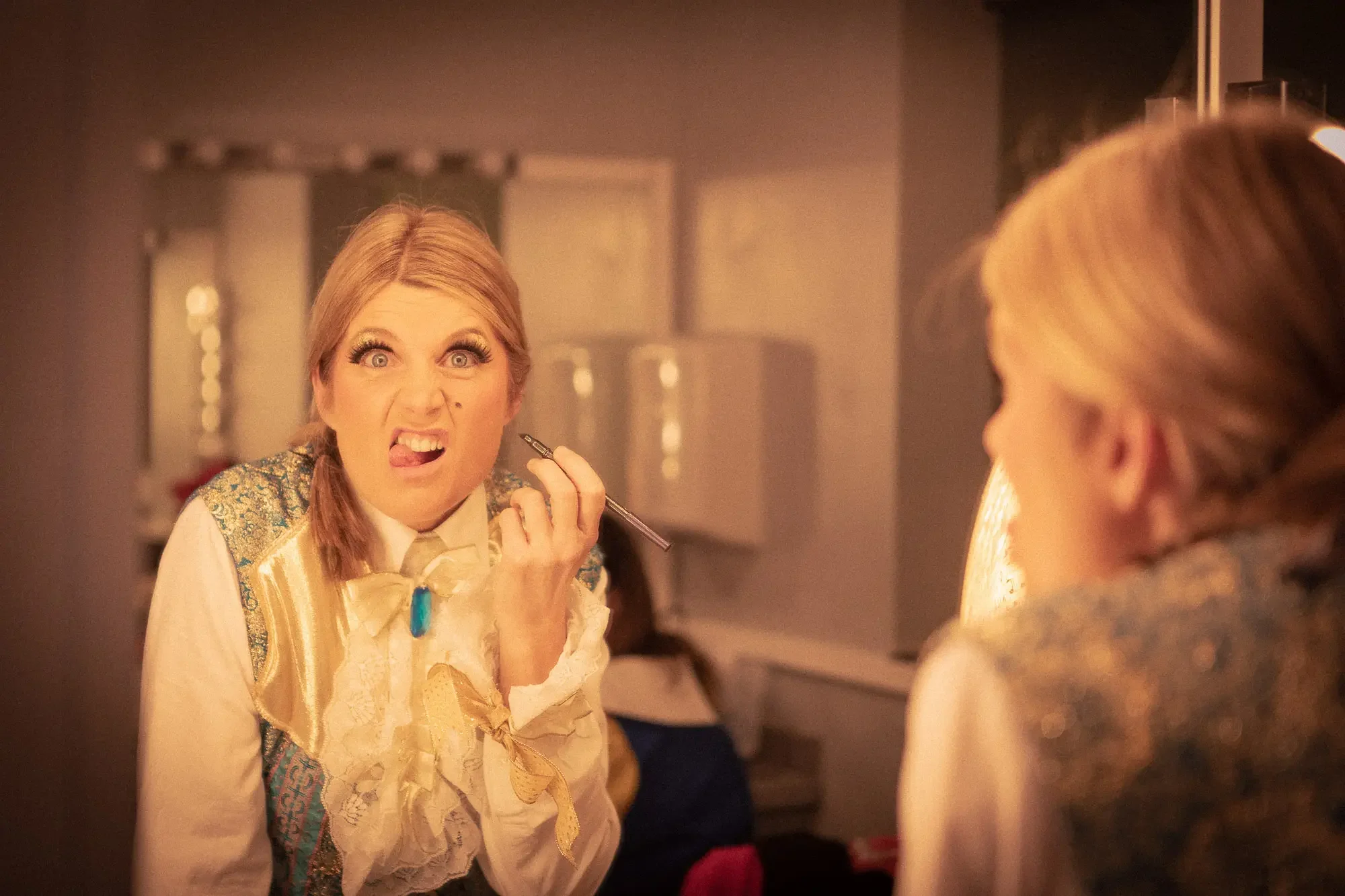 Panto-character-dressed-as-a-prince-applies-makeup-in-dressing-room.webp