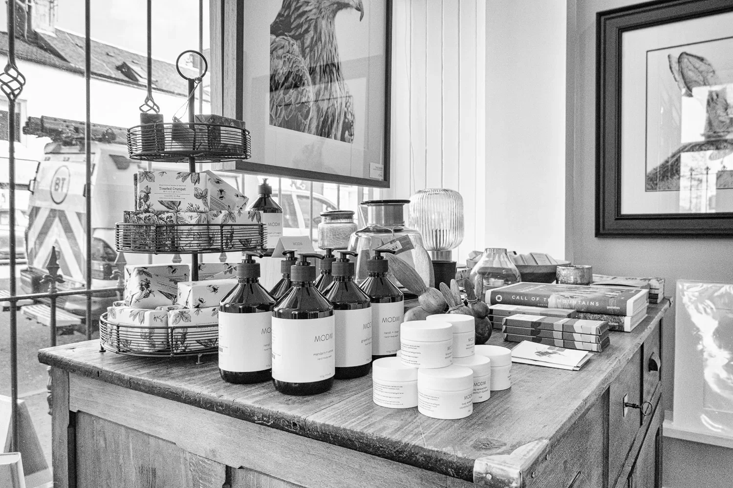  The product display on the main dresser — MODM skincare bottles, art books, glassware, and a large framed pencil portrait of a golden eagle dominating the wall behind. Interior detail shots like this one build the atmosphere of a brand. They show a 