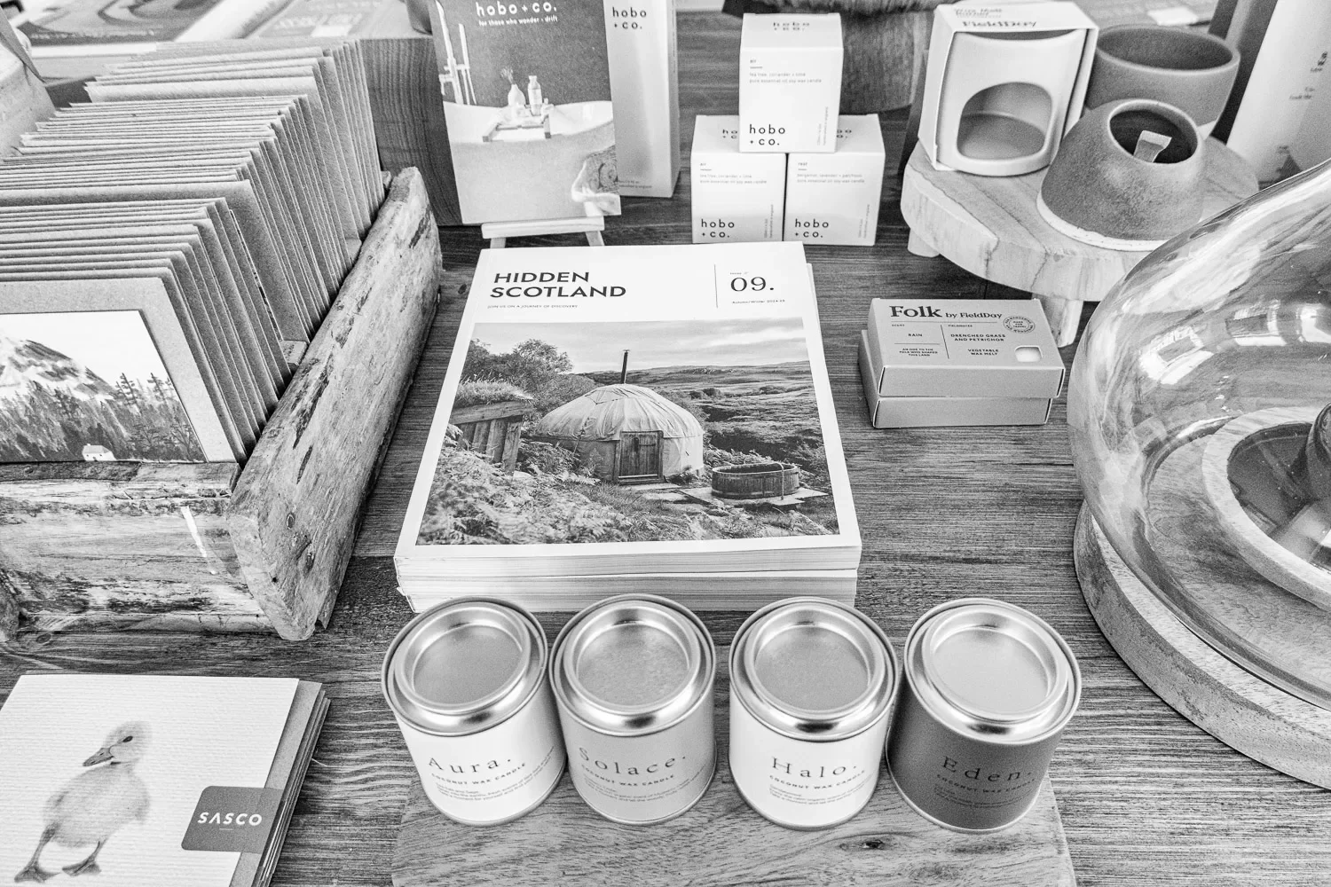  The retail display table: a copy of  Hidden Scotland  magazine, Hobo + Co products, Folk by FieldDay, and four coconut wax candles — Aura, Solace, Halo, Eden — lined up in a row. The details matter. These images aren't background filler; they're the