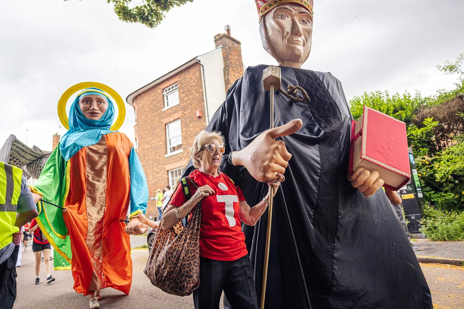  Two giant puppets representing saints processing through the streets of St Albans during the Alban Day 2026 pilgrimage, with a pilgrim walking between them, Hertfordshire. 