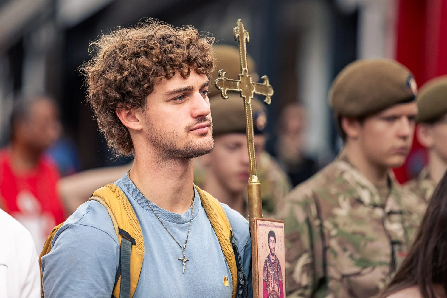  Young male pilgrim carrying a golden processional cross and Saint Alban icon during the Alban Day 2026 pilgrimage in St Albans, Hertfordshire, with soldiers visible behind him. 