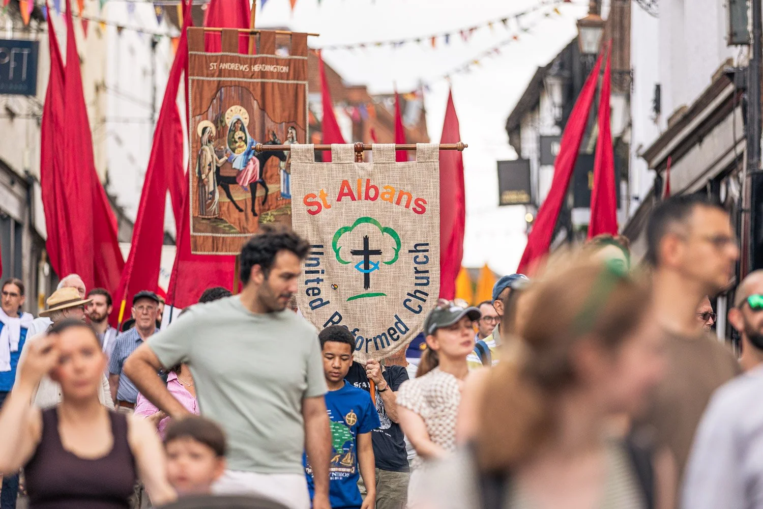  Crowd of pilgrims and church banners including St Albans United Reformed Church filling the decorated streets of St Albans city centre during the Alban Day 2026 procession, Hertfordshire. 