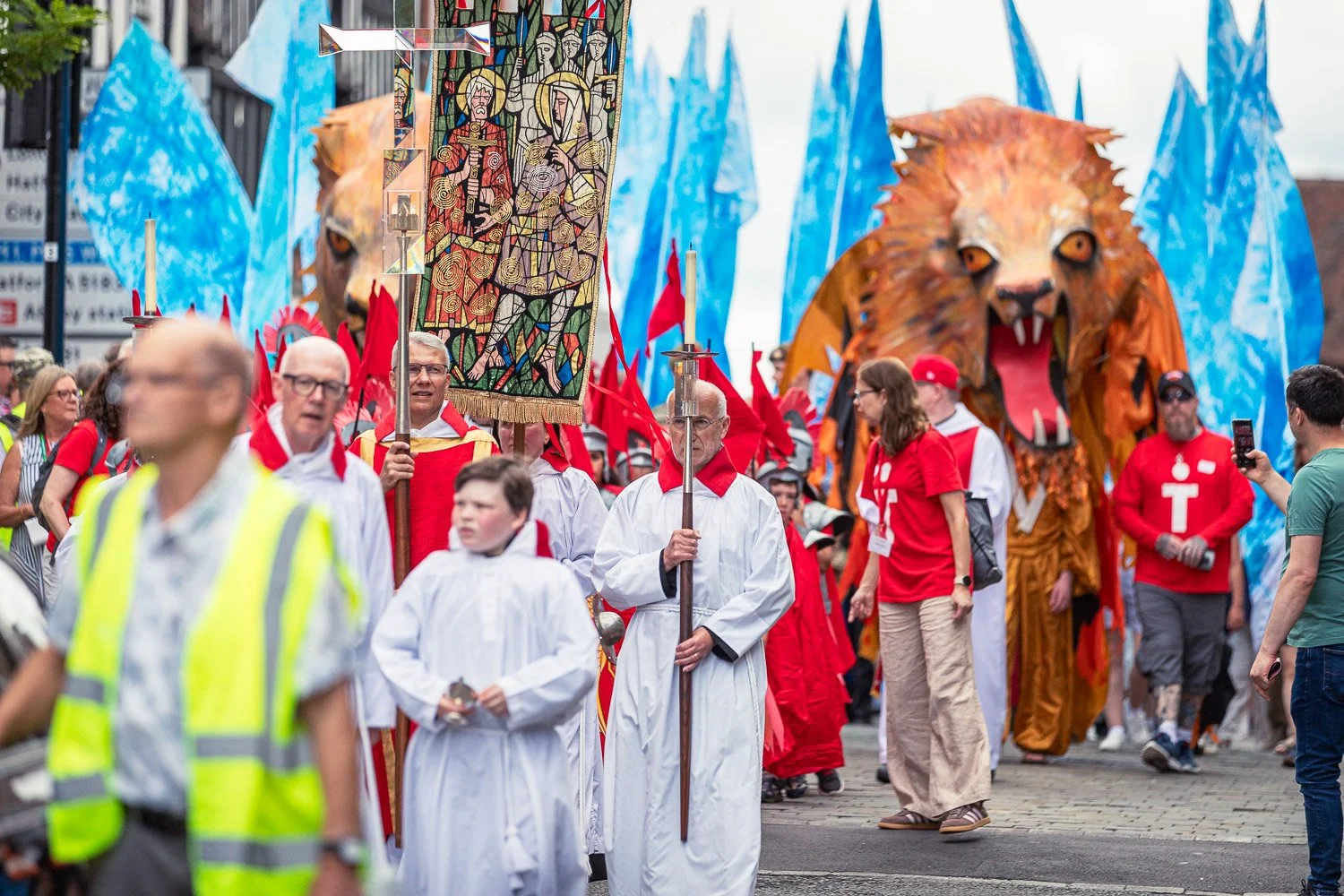  Clergy and pilgrims processing through St Albans with a giant lion puppet, blue flags, and a decorated tapestry banner during the Alban Day 2026 pilgrimage, Hertfordshire. 