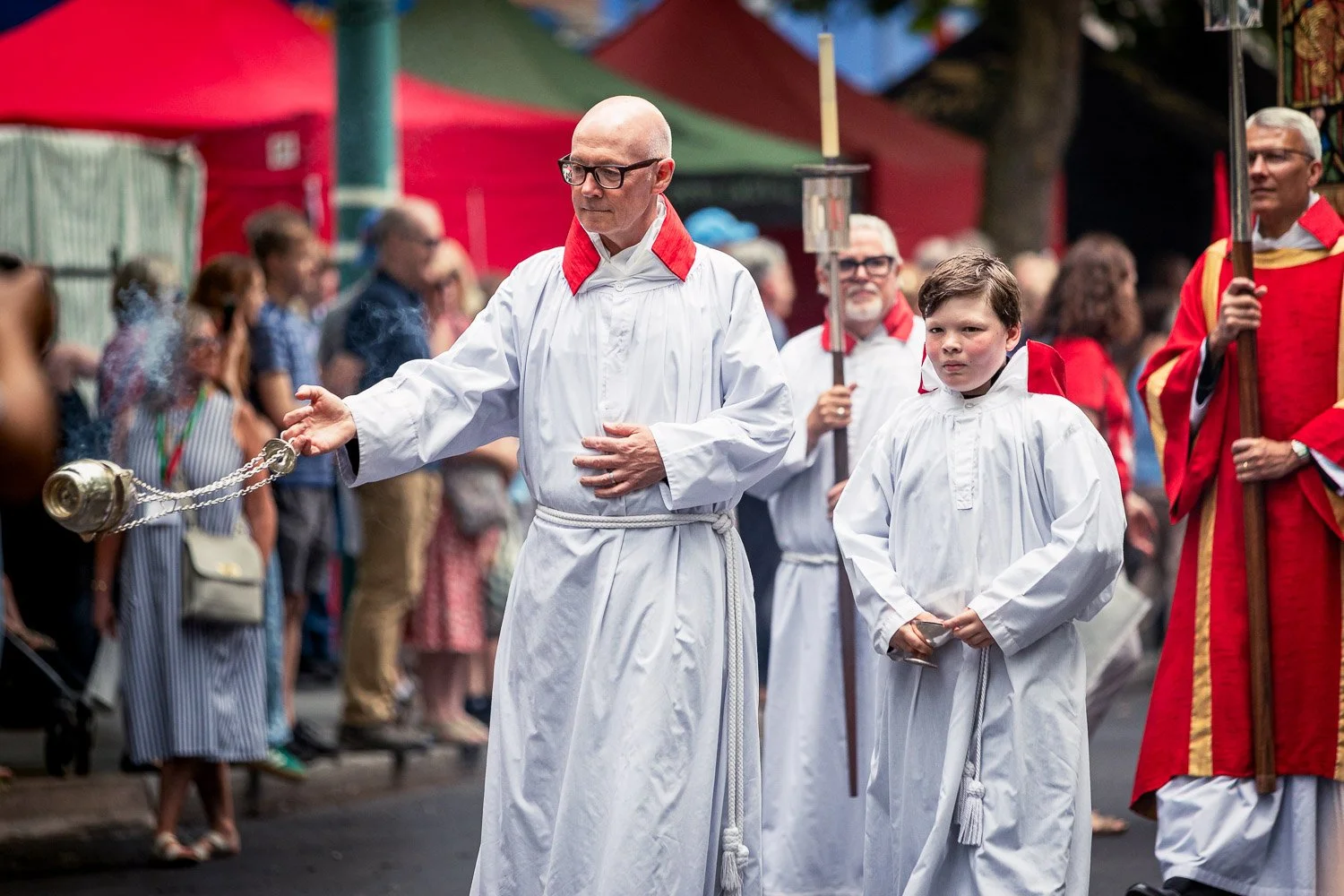  Thurifer in white robes swinging an incense censer during the Alban Day 2026 pilgrimage procession in St Albans, Hertfordshire, with a chorister and clergy visible behind. 
